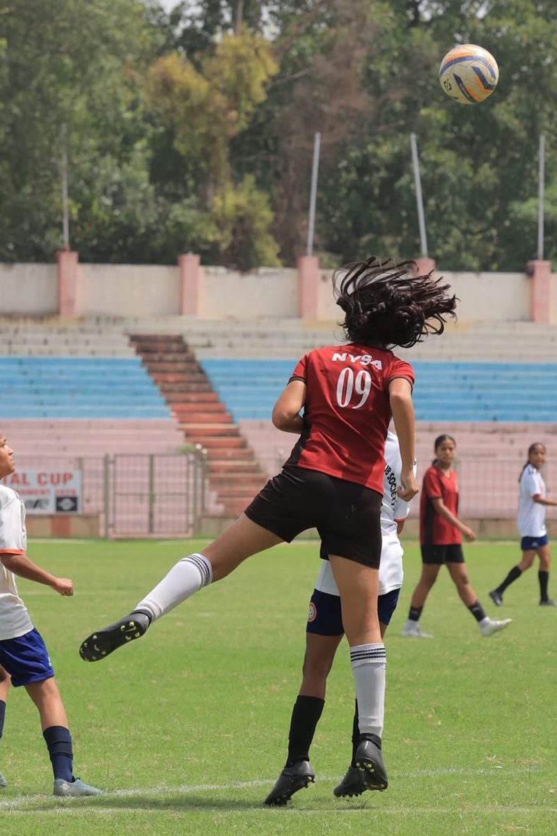 Nysa Bedi, number 09 in a maroon kit, leaping to head a football during a match