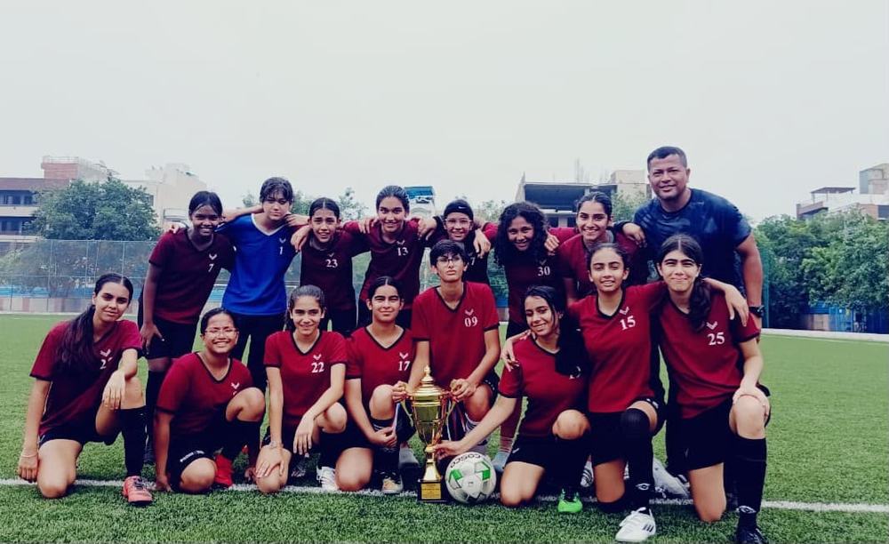 The Vasant Valley girls' football team in maroon kit with a gold trophy and a ball