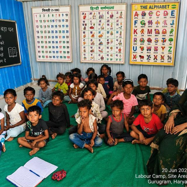 Children seated on a mat in a labour camp classroom with alphabet charts behind them